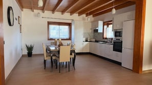 Eine moderne Küche mit weißen Schränken, einem Essbereich inklusive Tisch und Stühlen sowie einer Holzbalkendecke.