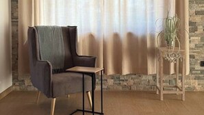 Um quarto com parede de pedra, uma cadeira, uma mesa e uma cortina.