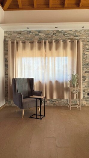Ein Zimmer mit Steinwand, einem Stuhl, einem Tisch und einem Vorhang.