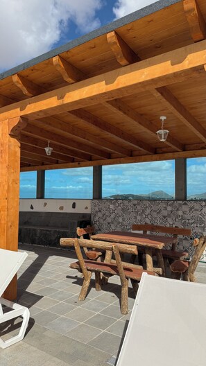 Eine Terrasse im Freien mit Holztischen und -bänken, Steinmauern und Blick zum Himmel.