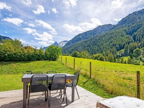 Ein Essbereich im Freien mit Tisch und Stühlen, mit Blick auf ein grünes Feld und Berge.