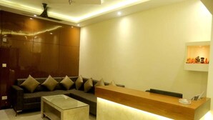 A modern reception area with a wooden reception desk, a sofa with multiple cushions, and a glass coffee table. - MM TAJ STAY (Fatehabad)