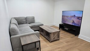 Una sala de estar moderna con un sofá seccional gris, una mesa de centro de madera y un televisor de pantalla plana sobre un soporte negro.