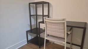 Una habitación con una silla blanca y un estante metálico negro adosado a una pared blanca.