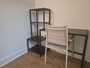 A room with a white chair and a black metal shelf unit against a white wall.