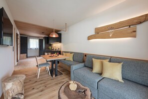 A modern living room with a sofa, a dining table, and a kitchen area in the background. - Knöspele Brennerei & Genuss-Apartments Fructum (Brixen)