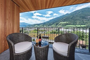 Ein Balkon mit Korbstühlen und einem Tisch, mit Blick auf eine gebirgige Landschaft.