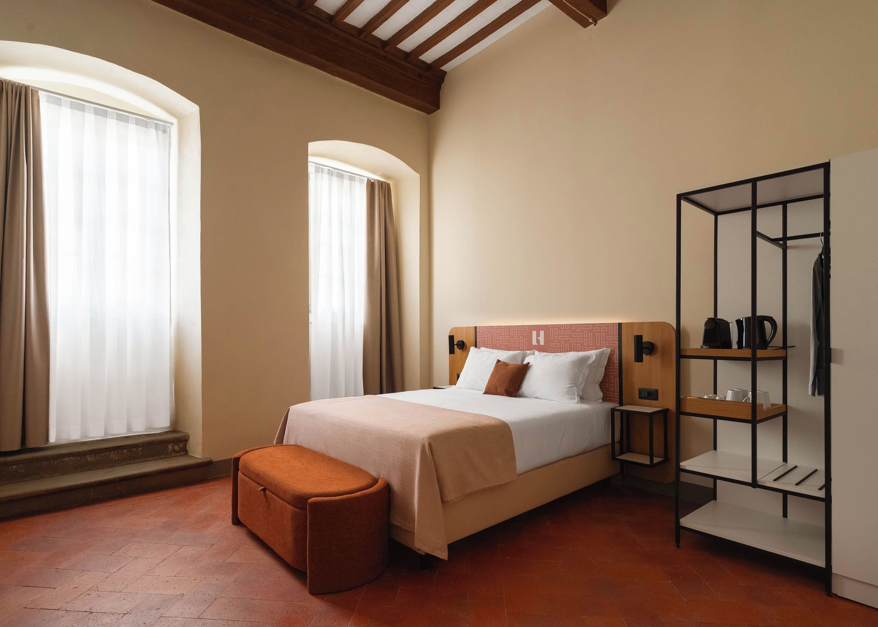 A hotel room with a bed, a bench, a wardrobe, and a shelf with items.