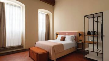A hotel room with a bed, a bench, a wardrobe, and a shelf with items.