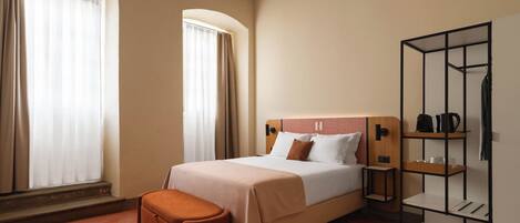 A hotel room with a bed, a bench, a wardrobe, and a shelf with items.