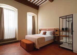 A hotel room with a bed, a bench, a wardrobe, and a shelf with items.