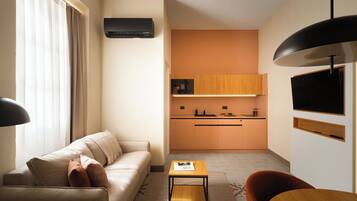A compact living space with a sofa, a small table, a kitchen area, and a TV mounted on the wall.