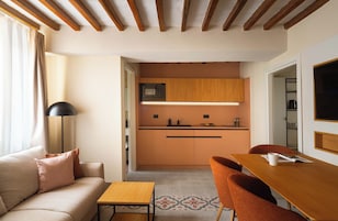 Un espacio habitable compacto con kitchenette, sofá, mesa de comedor y televisor.