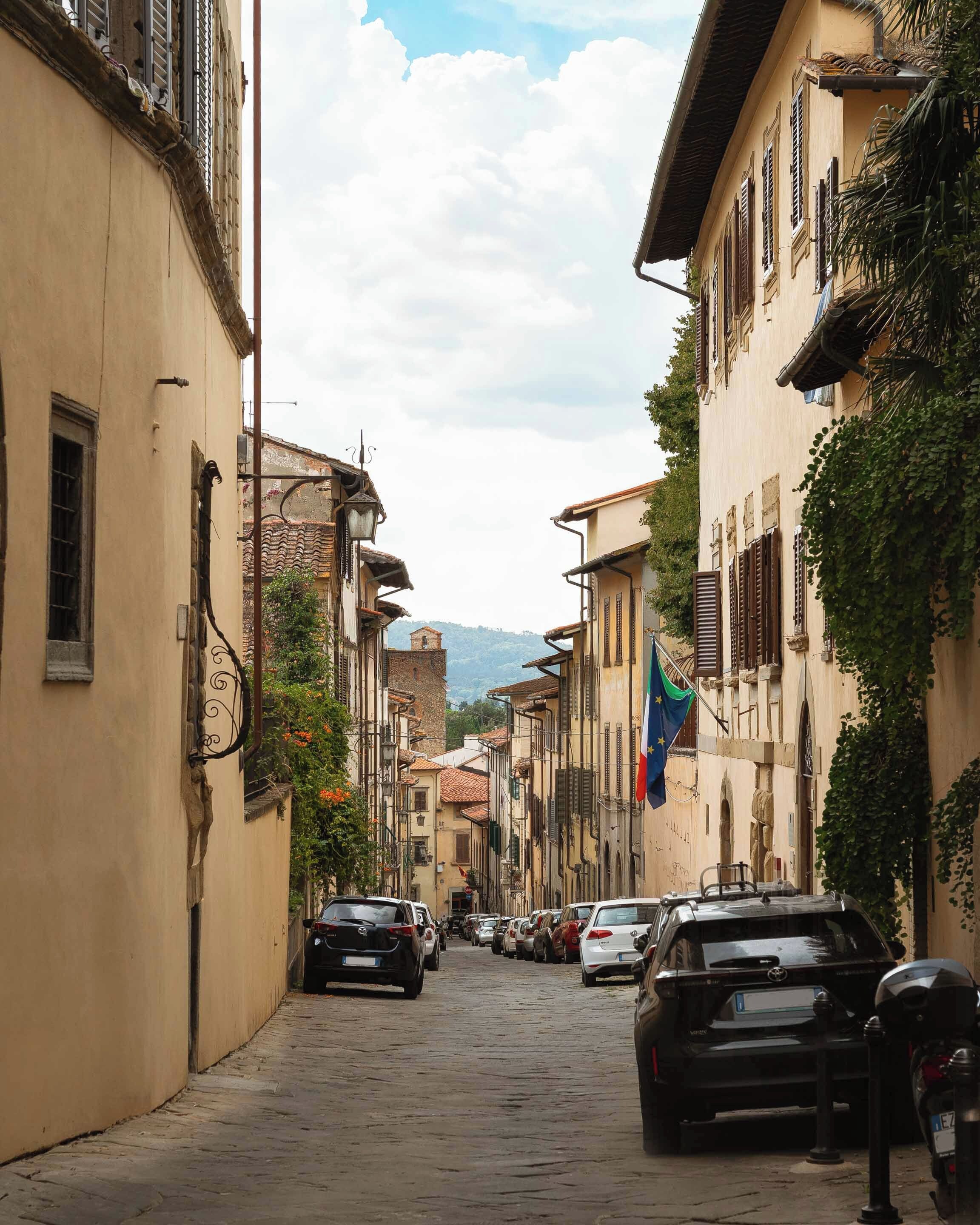 Una stretta strada acciottolata, con edifici dai balconi e bandiere, che evoca un'ambientazione europea.