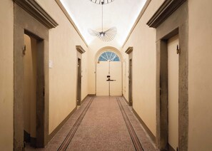 A hallway with a patterned carpet, a ceiling fan, and a door with a frosted glass window at the end.