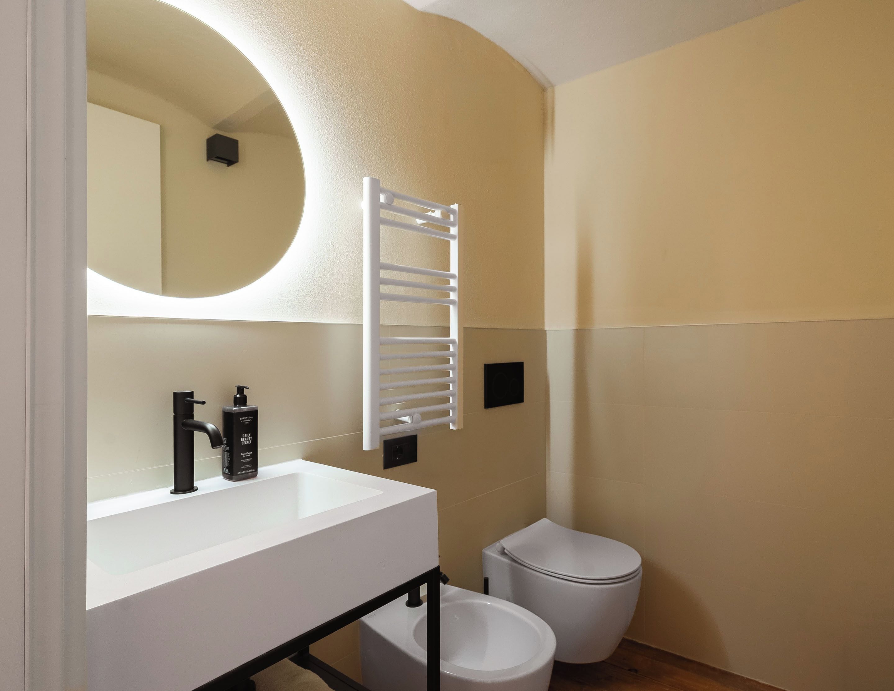 A modern bathroom with a white sink, black faucet, and a white toilet.
