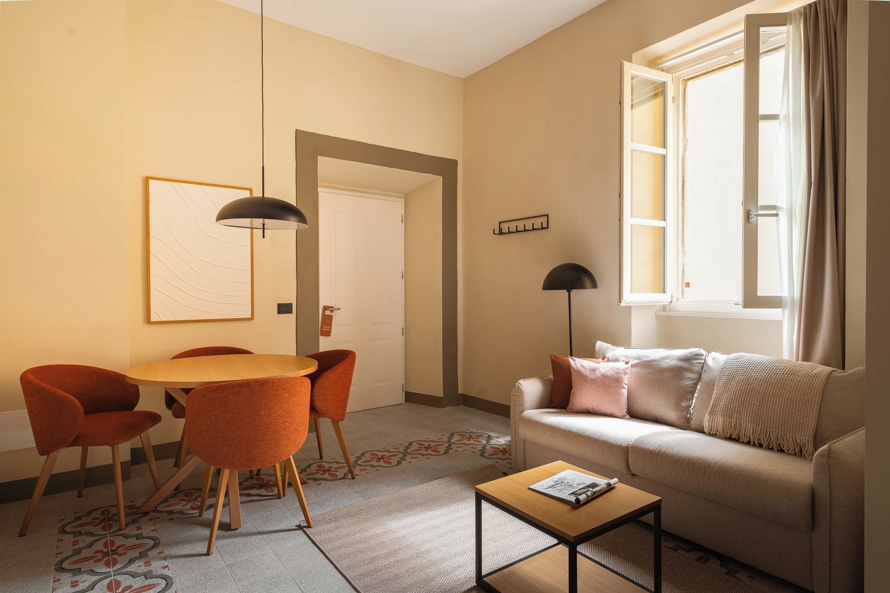 A living room with a sofa, a coffee table, a dining table with chairs, and a window with curtains.
