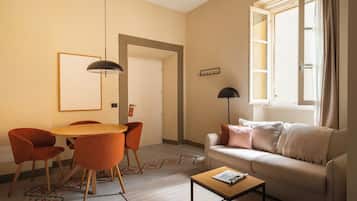 A living room with a sofa, a coffee table, a dining table with chairs, and a window with curtains.