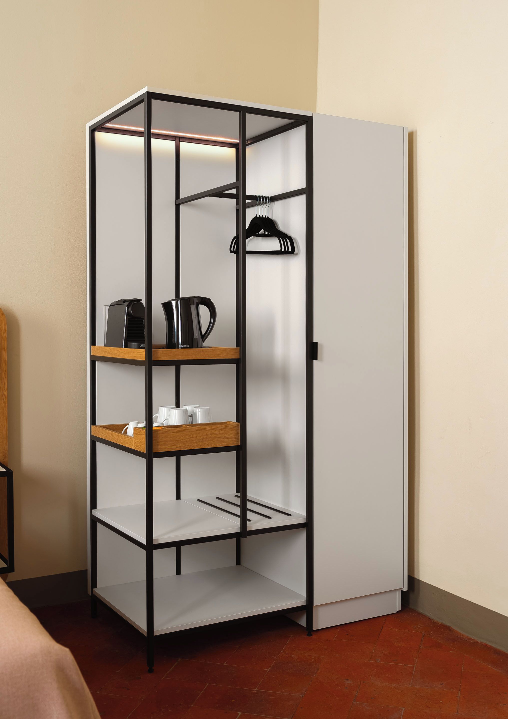A corner wardrobe with multiple shelves and a hanging rod, equipped with a kettle and cups.