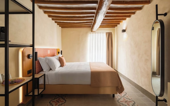 A hotel room with a bed, a bedside table, a mirror, and a ceiling with wooden beams.