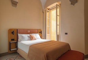 A hotel room with a bed, bedside table, and a window with curtains.