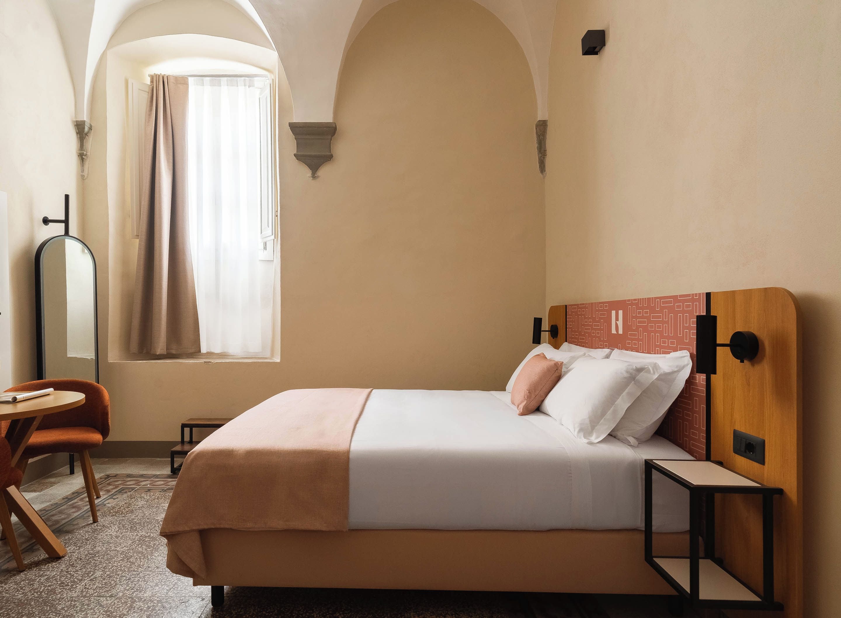 A hotel room with a bed, a chair, a table, and a window with curtains.