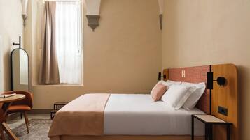 A hotel room with a bed, a chair, a table, and a window with curtains.