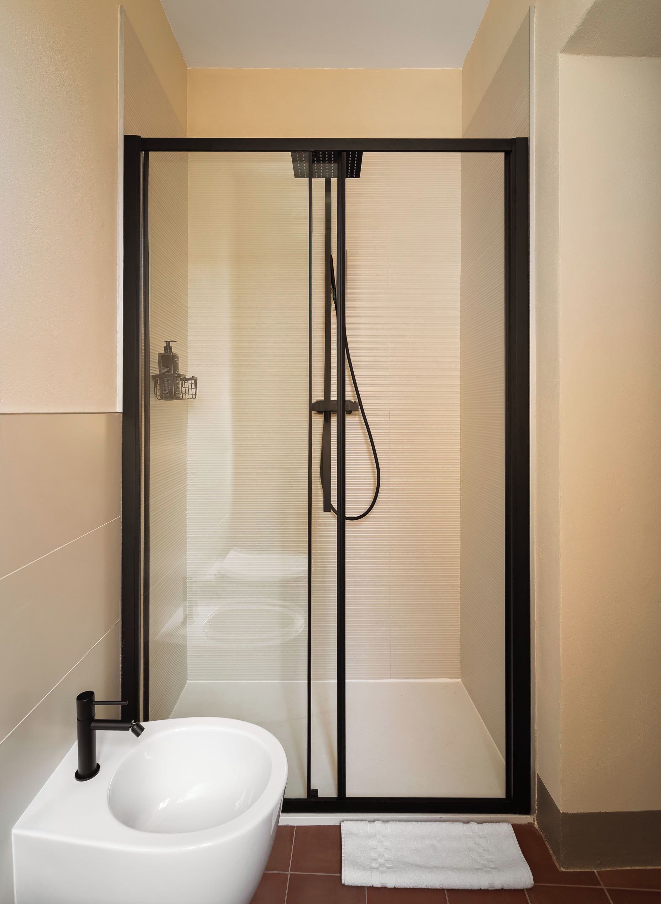 A modern bathroom with a glass-enclosed shower, a white sink, and a towel on the floor.