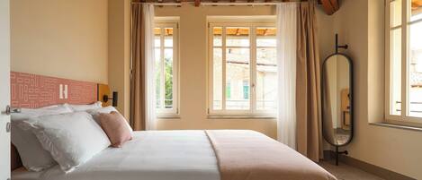 A bedroom with a bed, a bedside table, a mirror, and windows with curtains.