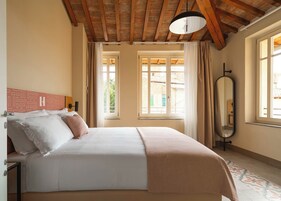 Un dormitorio con cama, mesita de noche, espejo y ventanas con cortinas.