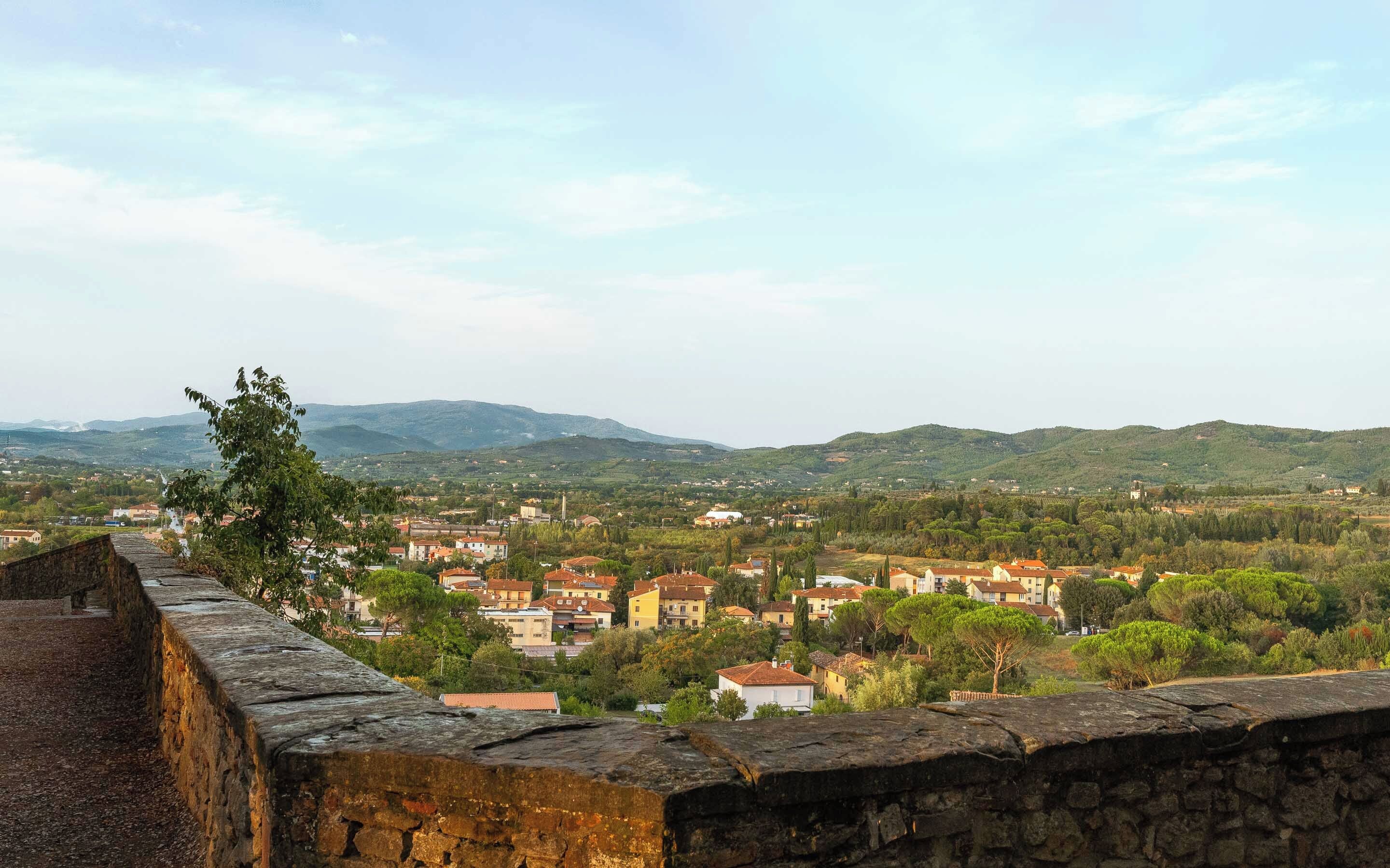 A stone wall overlooking a town with buildings and hills in the distance.
