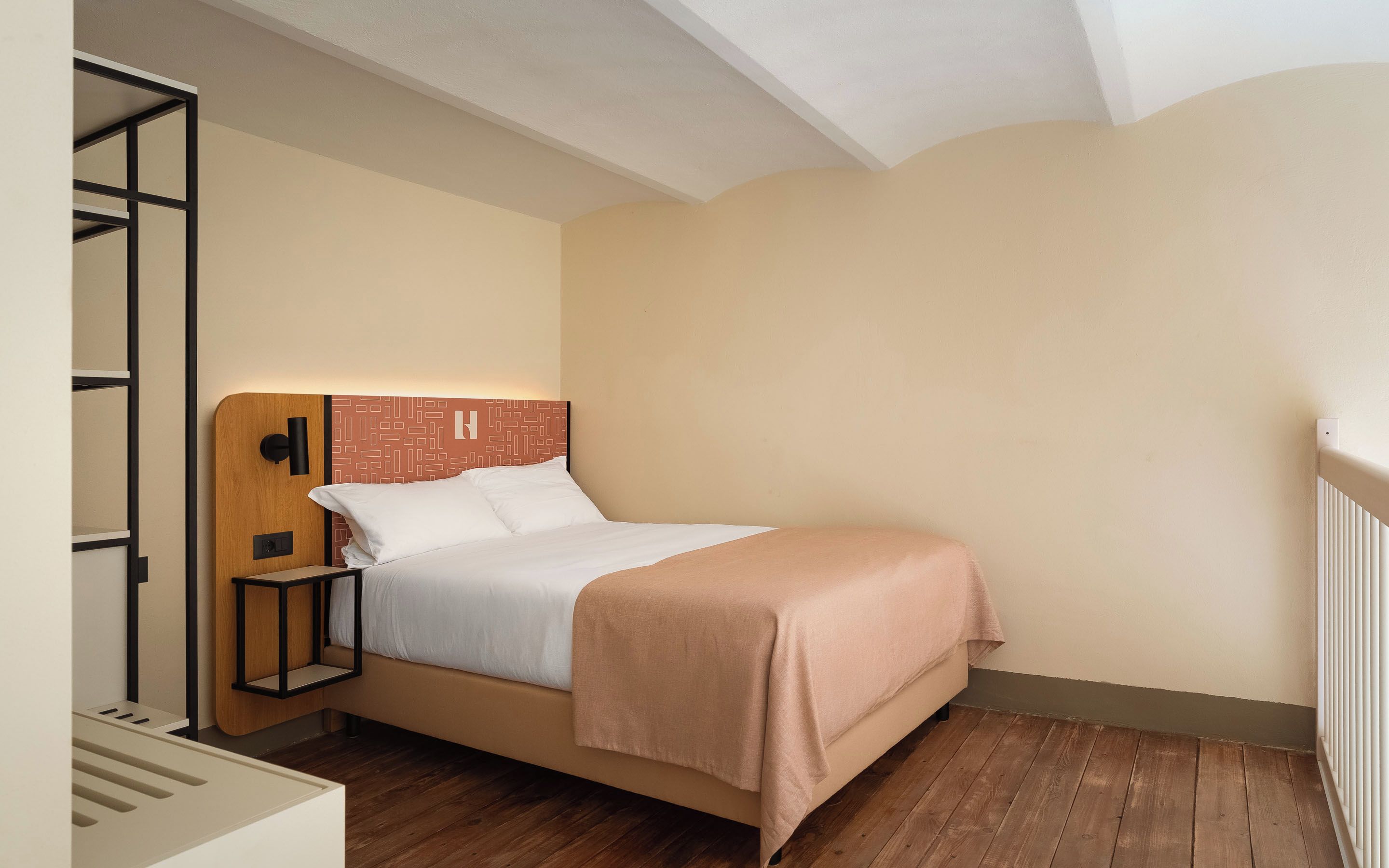 A single bed with a wooden headboard, a bedside table, and a wall-mounted light fixture.