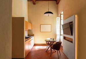 A compact kitchen with a dining area, a pendant light, and a framed artwork on the wall.