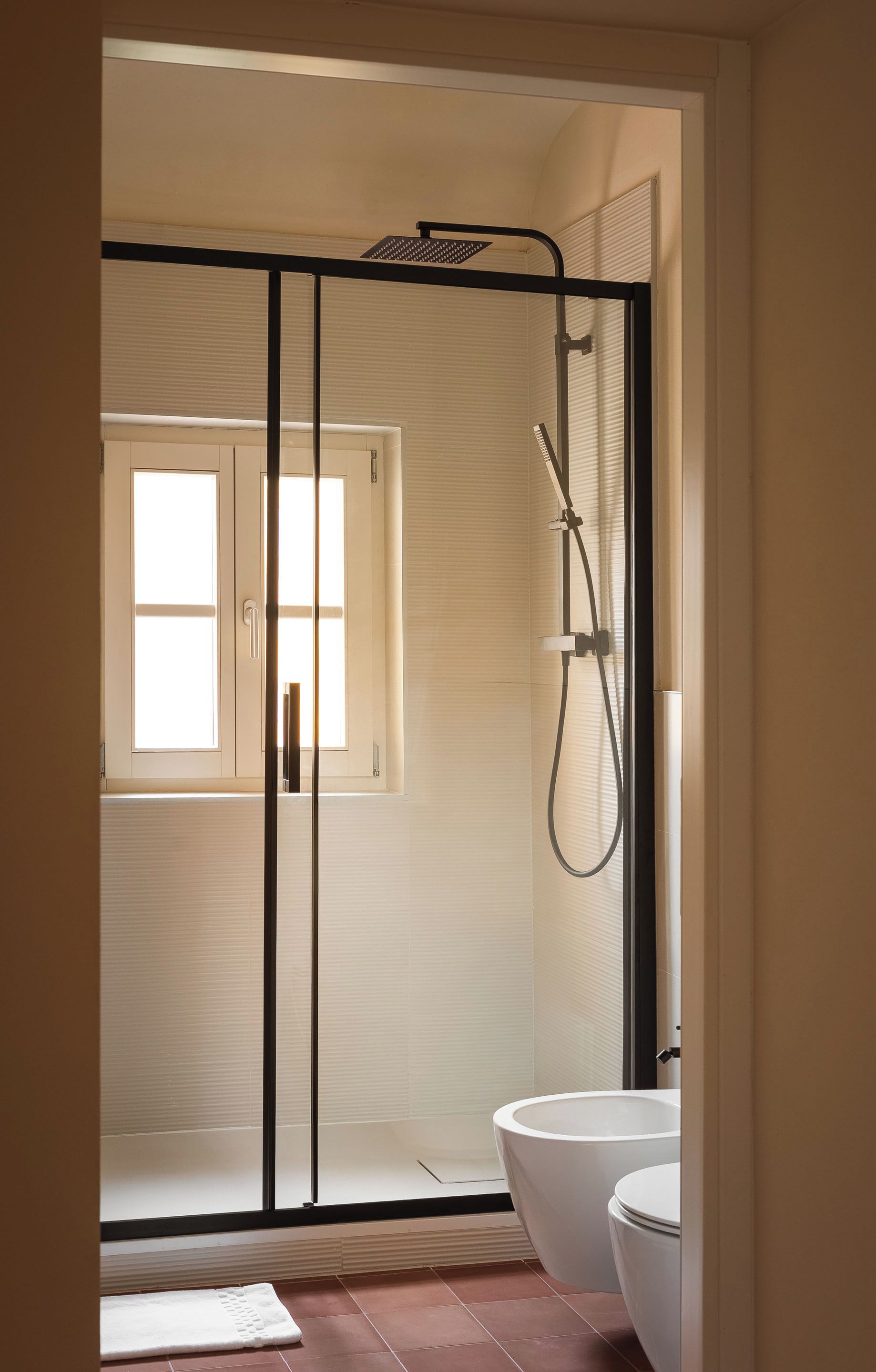 Ein modernes Badezimmer mit einer Duschkabine, einer weißen Toilette und einem großen Fenster.