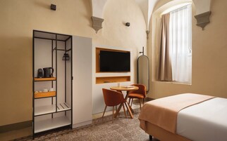 Habitación de hotel con cama, escritorio con silla, armario, televisión y ventana con cortinas.