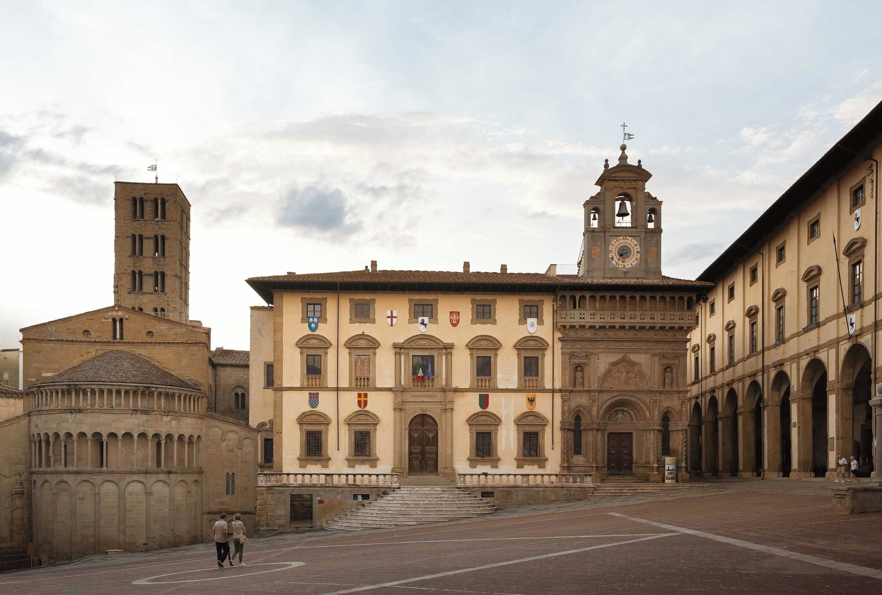 A historic building with a central courtyard, a bell tower, and multiple flags.