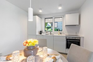 Una cocina moderna con armarios blancos, horno empotrado y ventana con vista a zonas verdes.