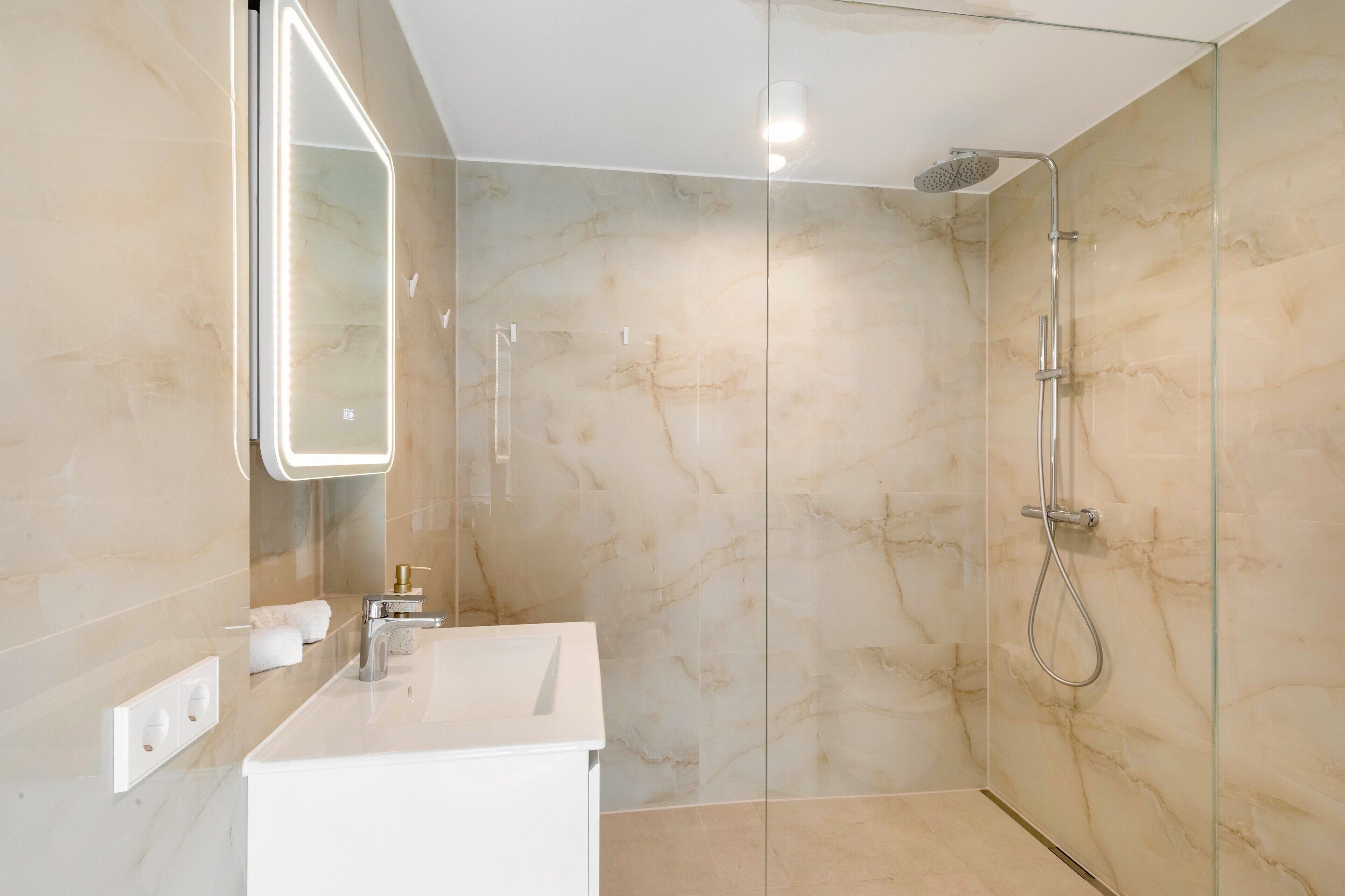Ein modernes Badezimmer mit einer gläsernen Dusche, einem weißen Waschbecken und einem Spiegel mit integrierter Beleuchtung.