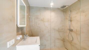 Ein modernes Badezimmer mit einer gläsernen Dusche, einem weißen Waschbecken und einem Spiegel mit integrierter Beleuchtung.
