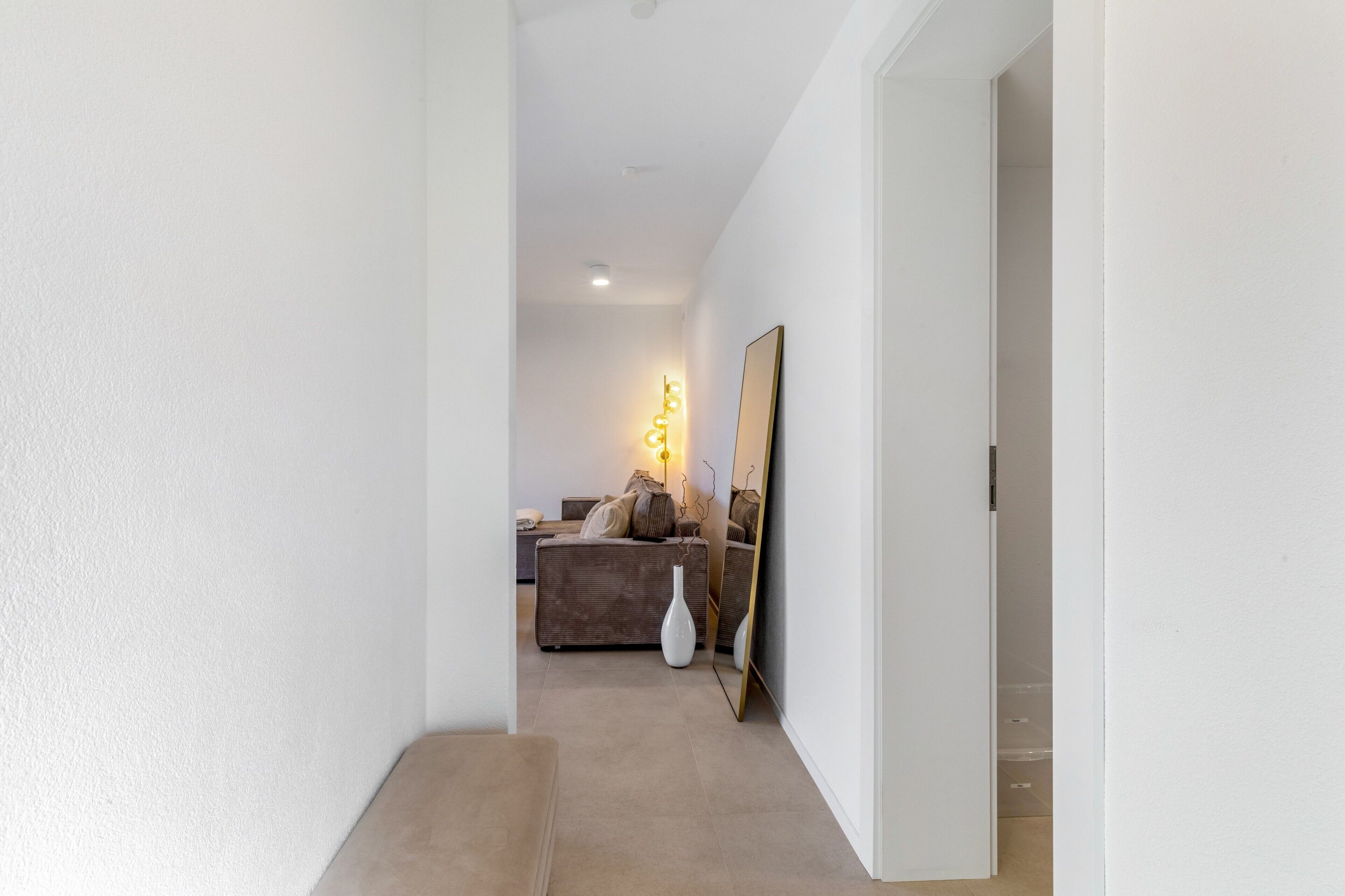 A hallway leading to a living area with a sofa, a lamp, and a mirror.