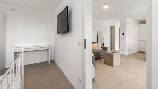 Ein modernes Interieur mit einem an der Wand befestigten Flachbildfernseher, einem weißen Konsolentisch und einer Treppe mit weißer Handläufer.