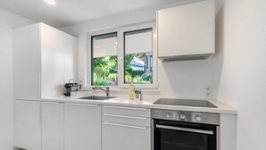 Eine moderne Küche mit weißen Schränken, einer Edelstahlspüle, einem Einbauofen und einem Fenster mit Blick auf Grünflächen.