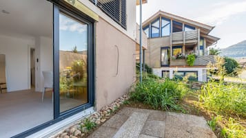 A modern building with a glass door entrance, a balcony with plants, and a stone pathway leading to the entrance.