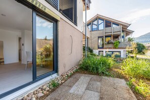 A modern building with a glass door entrance, a balcony with plants, and a stone pathway leading to the entrance.