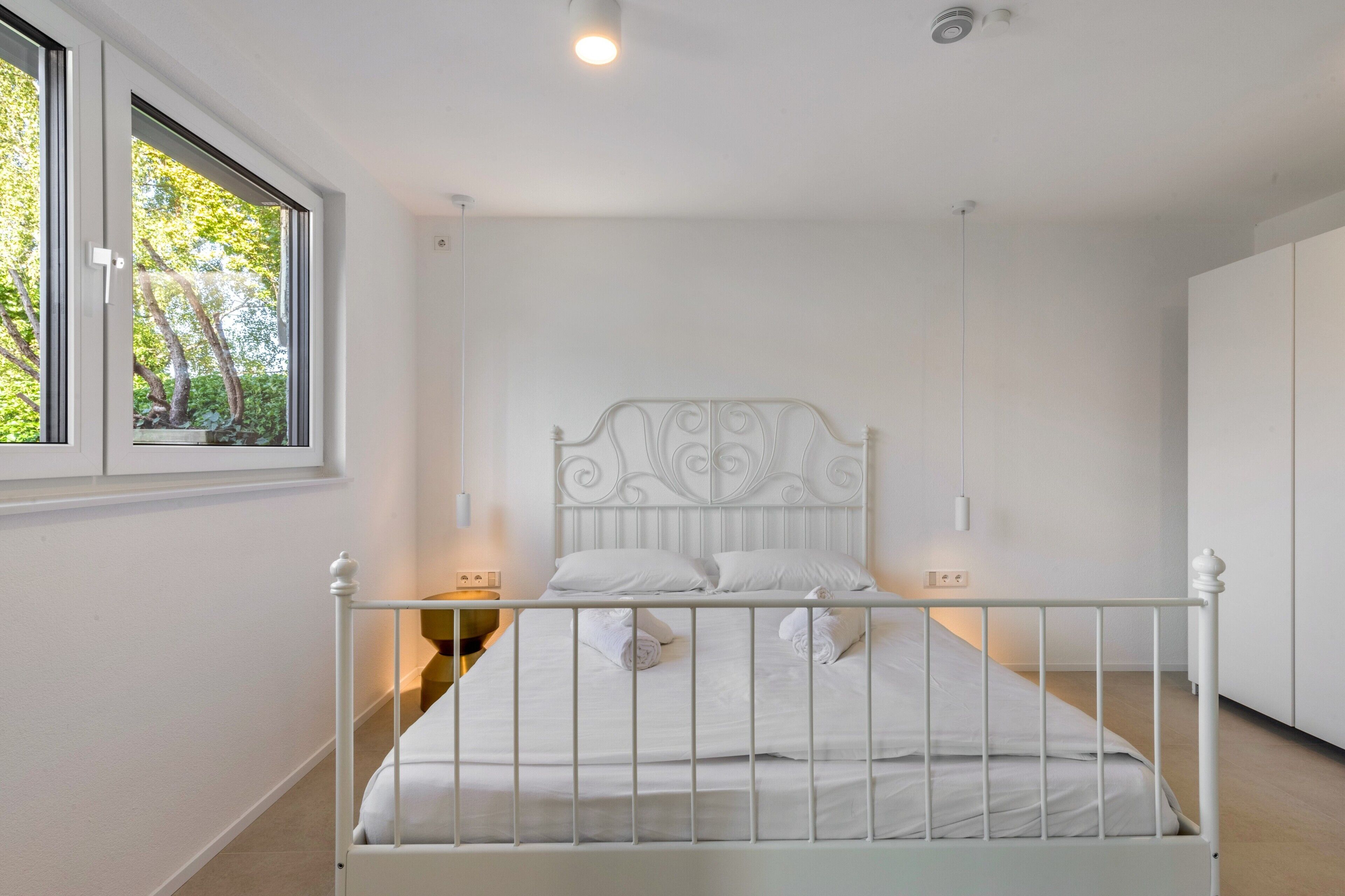 A bedroom with a white metal bed frame, a window with a view of trees, and a white wall.