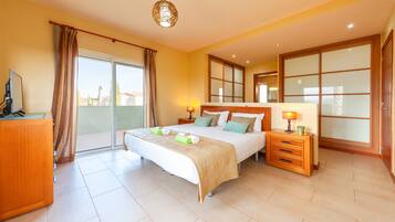 A hotel room with a bed, bedside tables, a desk, and a sliding glass door to a balcony.