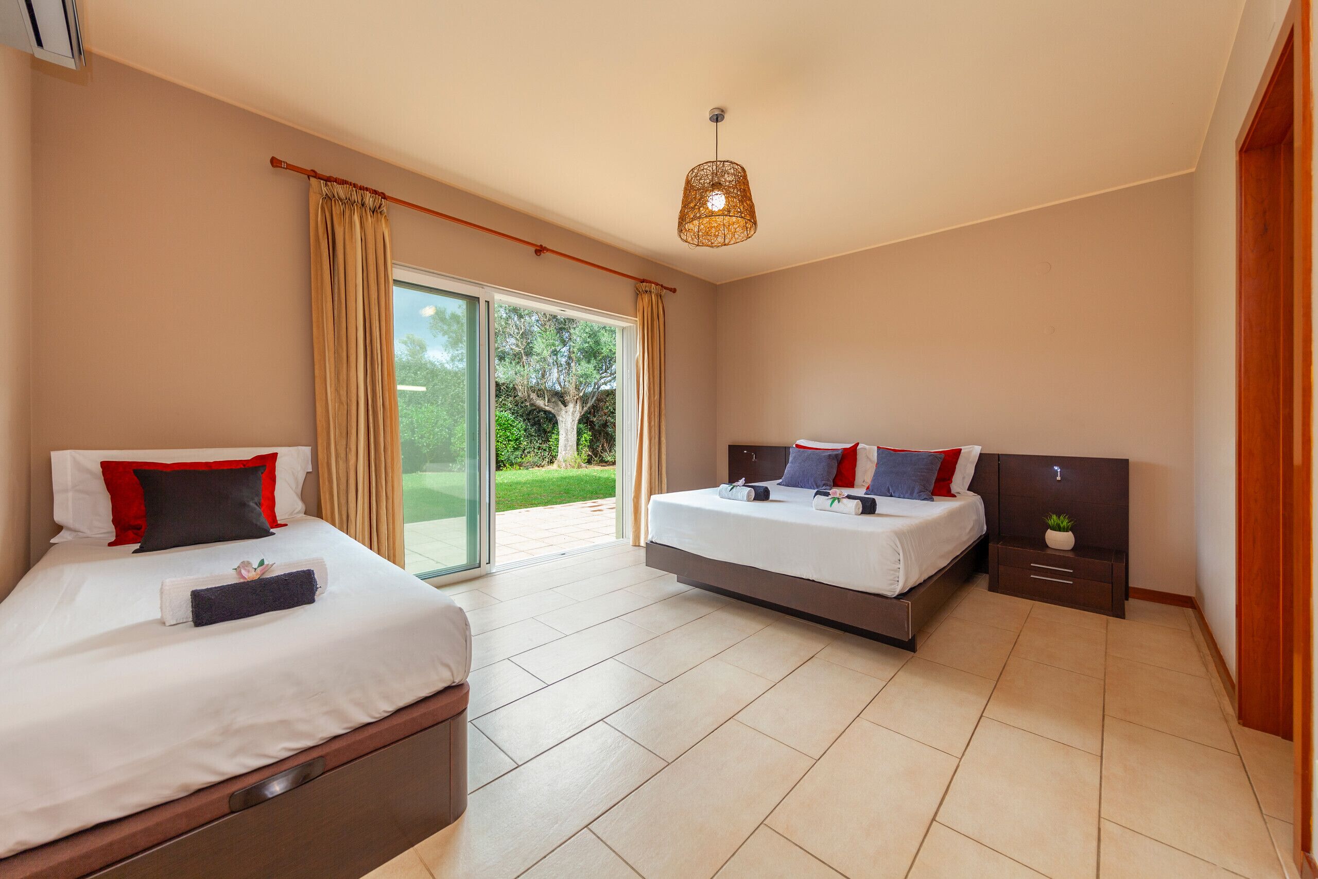 A modern hotel room with two beds, a large sliding glass door to the outdoors, and a ceiling light fixture.