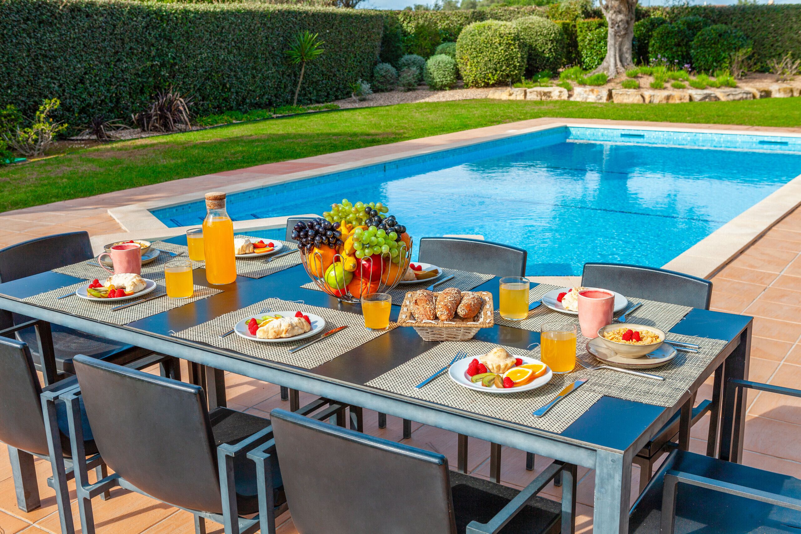 A dining table set with breakfast items and beverages by a poolside.