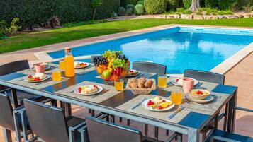 A dining table set with breakfast items and beverages by a poolside.