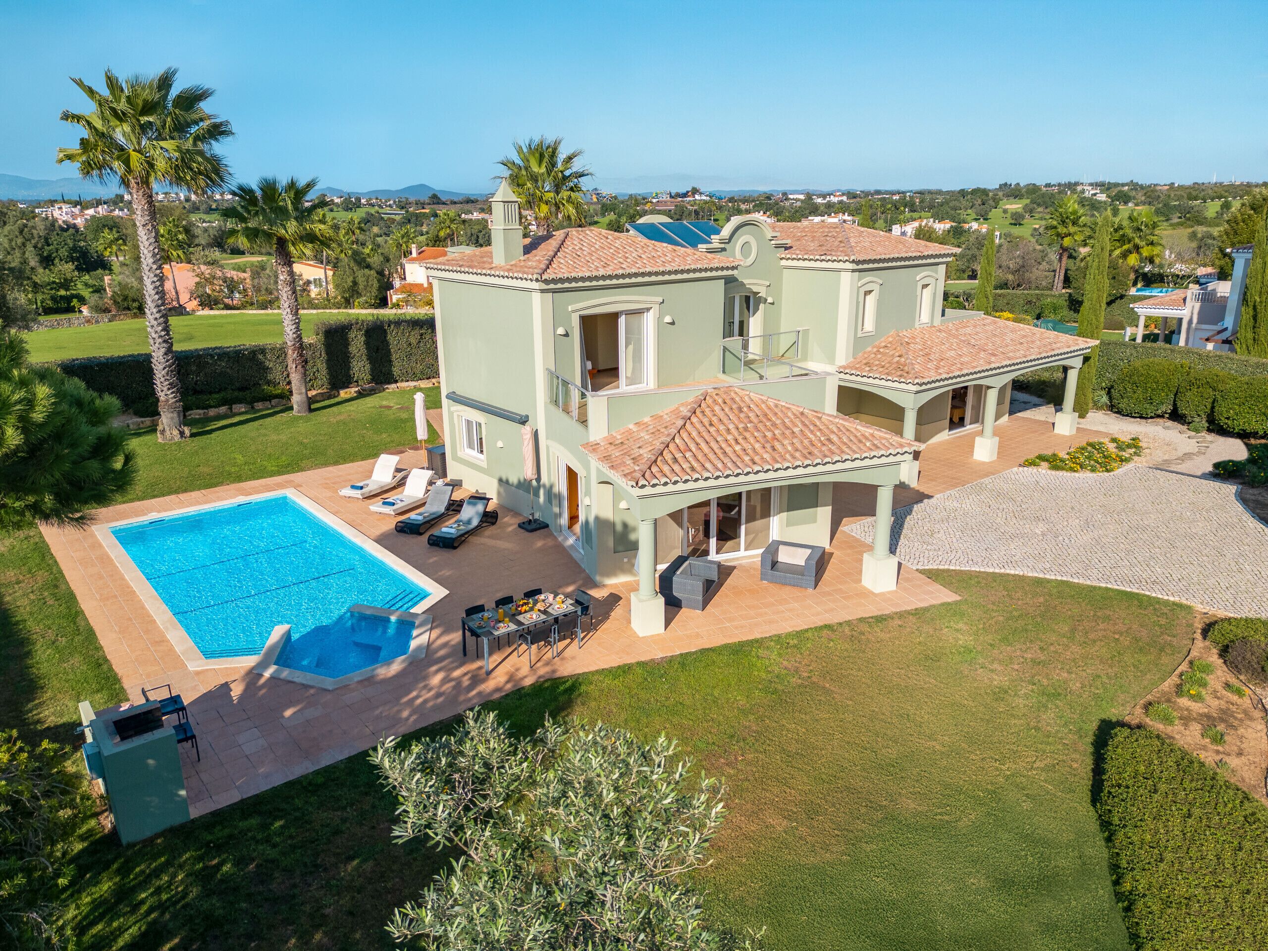A large house with a swimming pool, outdoor seating, and a view of the surrounding landscape.